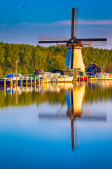 Naklejka na ściany i meble Dutch Windmill In Front of The Canal With Moored Motorboats Located in Traditional Village in The Netherlands. Shot at Kinderdijk During Golden Hour.