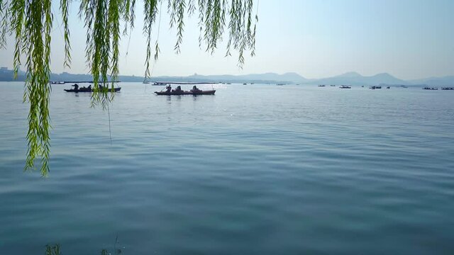 Visitors rent boats and paddle in lake of park. Willows swaying in breeze