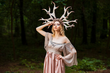 Obraz na płótnie Canvas Beautiful Caucasian Girl With Artistic Deer Horns In Forest. Posing in Light Dress for Demonstrating Forest Nymph Concept for Art Photography.