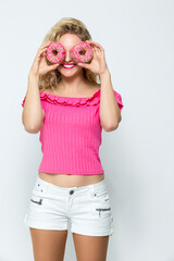 Food Ideas. Portrait of Funny Laughing Caucasian Blond Girl Holding Pink Doughnuts in Both Hands in Front of Her Face. Posing in Sexy White Shirts On White