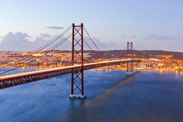 Fototapeta na wymiar Portugal Travel Destinations. Crossing The Tagus River. Amazing Image of Lisbon Cityscape Along with 25th April Bridge (Ponte 25 de Abril). Taken from Almada District. Picture Taken at Twilight.