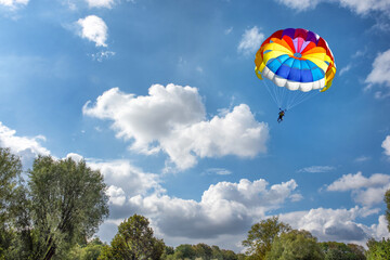 Paragliding using a parachute on background of green forest under blue cloudy sky.