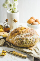 Homemade sourdough bread, some eggs, oil, sesame, wood cutting board, white background, wood knife and napkin.