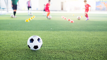 Soccer ball on green artificial turf with blurry kid soccer team training. Blurry kid soccer player...