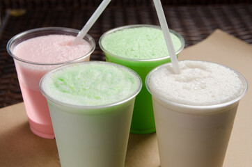 white, pink and green milkshakes in transparent cups with a straw