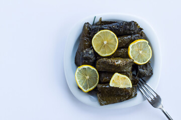 Traditional Turkish food stuffed with wet vine,grape leaves rolled in plate with sliced lemon and fork.Ready for eat.