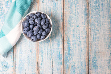 Fototapeta na wymiar Close up top down overhead shot of a white bowl of blueberries on a weathered, rustic, light blue wooden table