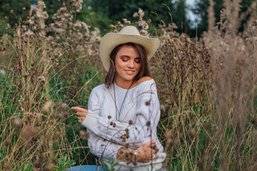 Young beautiful brunette woman sitting on the grass, smiling and touching her hair