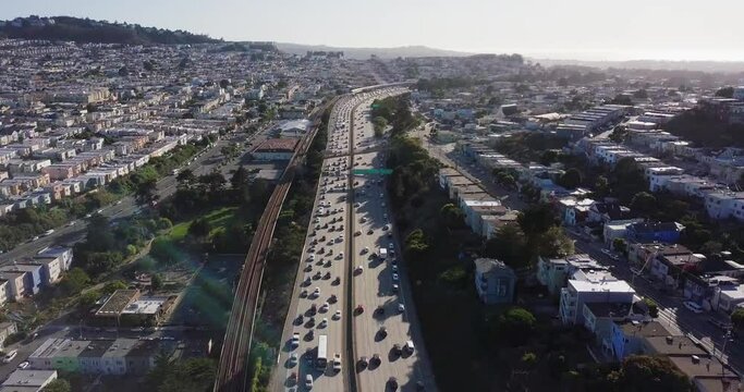 Highway traffic during sunset and cars going in opposite direction. Bart train on the track and muni on the road