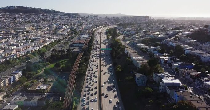 Highway traffic during sunset and cars going in opposite direction. Bart train on the track and muni on the road