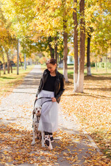 Fototapeta premium Ballerina with Dalmatian dog in the Park. Woman ballerina in a white ballet skirt and black leather jacket dancing in pointe shoes in autumn park with her spotty dalmatian dog.