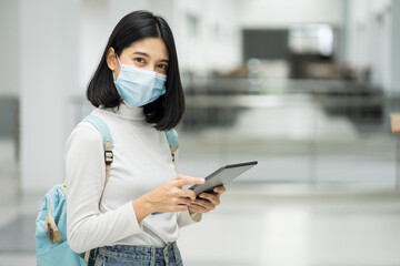 Portrait of a teenage college student wearing medical protective face mask with school backpack to protect from influenza virus, COVID-19 pandemic in college building