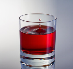 Stack of drops of wine flying in glass of red wine close up. High speed shot