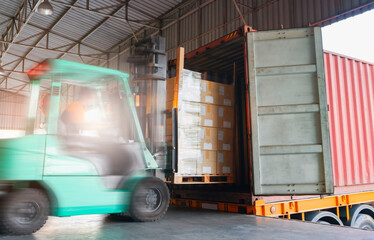 Motion blur of forklift driver loading cargo shipment pallet goods into a truck container at dock...