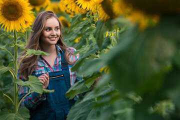 Gorgeous, energetic, female farmer standing in the middle of a beautiful green and golden sunflower field.