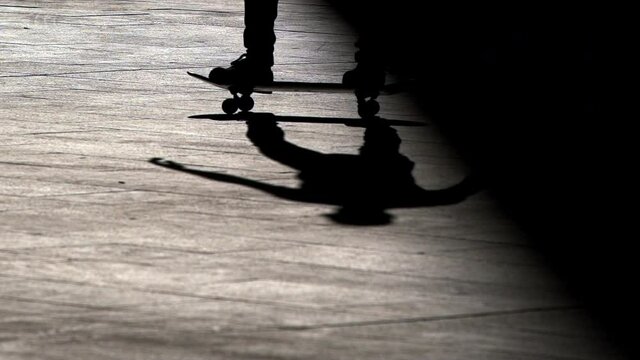 Skateboarder and biker rides on a fully backlit silhouette image within a beam light that cuts the image vertically. Artistic image. Skateboarder cross the light beam horizontally