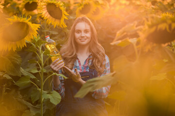 Gorgeous, female farmer holding a bottle of sunflower oil in the middle of a sunflower field during...
