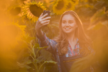 Young, adorable, energetic, female farmer taking a picture with herself in the middle of a beautiful sunflower field during a scenic sunrise.