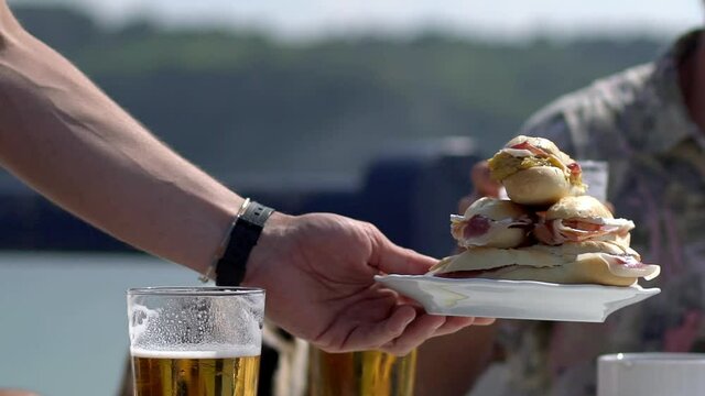 a group of friends on the Basque beach of Sopelana enjoy a sunset having some beers and some ham bread sticks. the image is a short detail where it is seen in the beers and the plate with appetizers