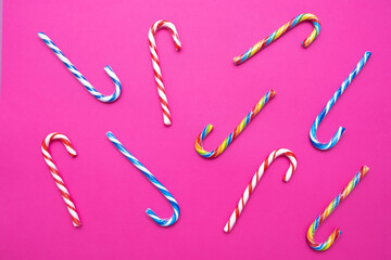 lot of multi-colored candy canes on a pink background, copy space