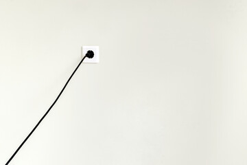 White electrical outlet with black wire and plug on a white wall in a city apartment.