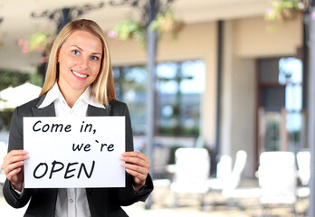 Happy woman holding a white banner with welcome sign. Come in, we are open