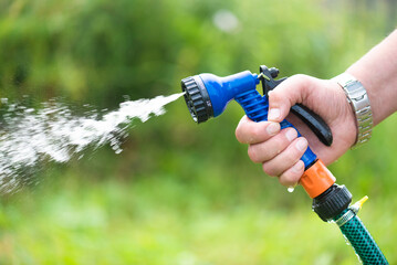 Gardener is watering a garden bed by a water sprinkler close up.