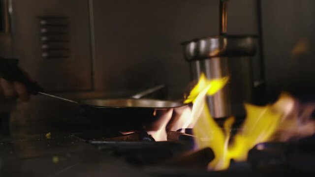 Chef cooking with flaming saucepan over hot stove