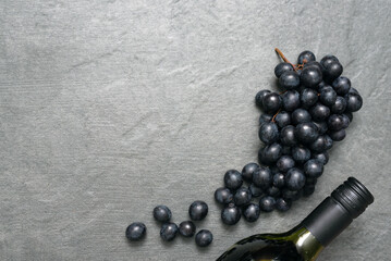 Bottle of red wine and grapes on stone surface flat lay background with copy space.