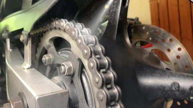 Oiling a motorcycle chain in a workshop. Closeup of spraying motorbike chain with oil lubricant. Mechanic is lubricating moto chain with lube.
