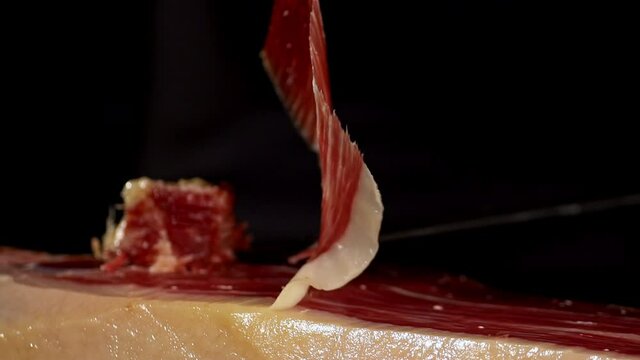 Tongs grabs a slice of Iberico ham, Jamon, that moves with the movement and is shown to the camera in a short image detail. Very appetizing to eat that delicacy, with impressive red and white colors