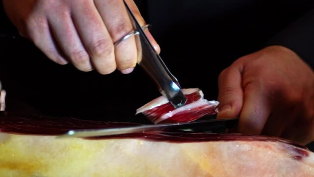 Ham cutter master  grabs  a slice of Iberico ham with his tongs,  in a short image detail. Very appetizing to eat that delicacy, with impressive red and white colors