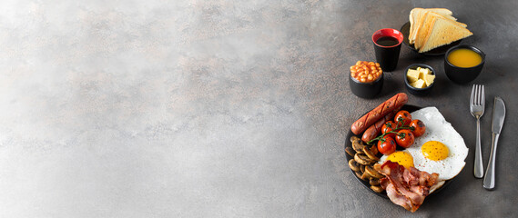 Typical English breakfast on large background for banner. Fried eggs, sausages, bacon, beans, mushrooms, toasts and butter, coffee and orange juice. Copy space