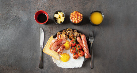 Top view of Full English breakfast  on concrete background.  Fried eggs, sausages, bacon, beans, mushrooms, toasts, butter, coffee, juice