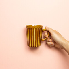 Female hand holding brown empty mug cup on pink background