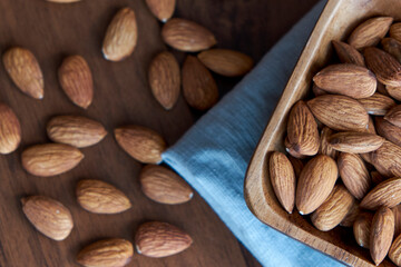Almonds in small wooden bowl. Almonds laid freely on dark table. Row of bowls with almond nuts, top view. Peeled almond pattern