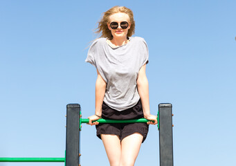 Happy young woman having a fun time at the outdoor playground hanging up on the bars during a sunny summer day.