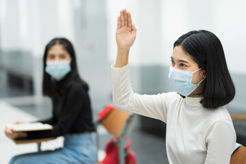 Teenage college students sitting in the class and raising hand up to participate ask question during lecture. High school student raises hand and asks lecturer a question.