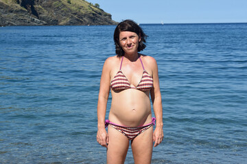 Obraz premium front view of pregnant woman standing on the beach looking at camera