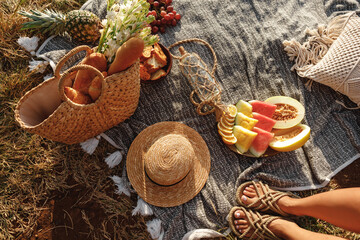 Beautiful summer picnic in boho style. Organic fresh fruits, wicker bag with baguettes and flowers on linen blanket. Picnic background with basket, fruits and wicker bag with baguette