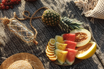 Beautiful summer picnic in boho style. Organic fresh fruits, wicker bag with baguettes and flowers on linen blanket. Picnic background with basket, fruits and wicker bag with baguette