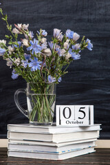 Flowers in a glass cup, books, glasses and calendar with the date of October 5, against background of chalkboard, Teacher's Day concept. Copy space.