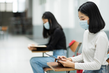 Female teenager college students wears face mask and keep distance while studying in classroom and college campus to prevent COVID-19 pandemic