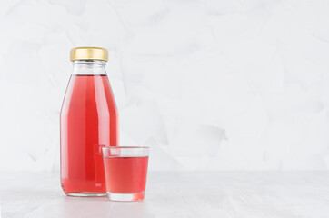Fresh pink fruit juice in glass bottle mock up with glass on wood table in white interior, template for packaging, advertising, design product, branding identity.