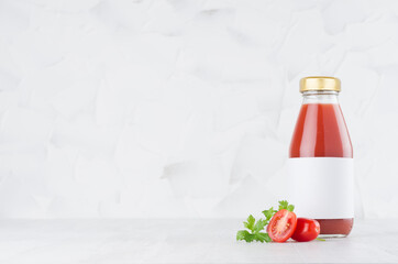 Fresh red tomato juice in glass bottle with blank label template with green parsley, vegetables...