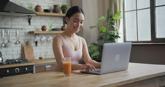 Healthy asian woman using laptop, texting message, drinking orange juice and smiling