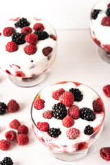 Delicious juicy berries of raspberries and blackberries with yoghurt in a glass form on a white background