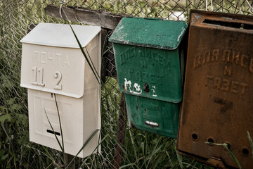 Vintage rustic mailboxes of different colors pinned on a fence.