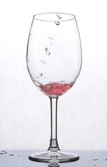 a glass with red liquid, which stands on a mirror surface, and is backlited, splashing