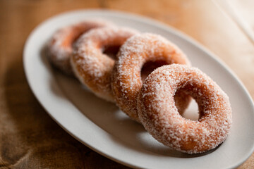 delicious sugar doughnuts on a white plate on a wooden board. the photo is very simple but looks very yummy. sugar doughnuts are easy to make and also perfcet for a snack or sugary breakfast.